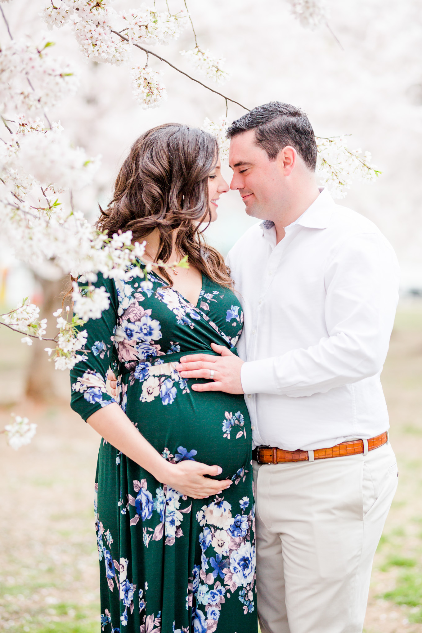 D.C. cherry blossoms maternity session, maternity portraits, maternity photos, D.C. cherry blossoms, cherry blossoms maternity photo, floral print dress, brunette expectant mom, expecting mother, brunette woman, pregnant woman, third trimester, baby bump, couple snuggling, cute couple
