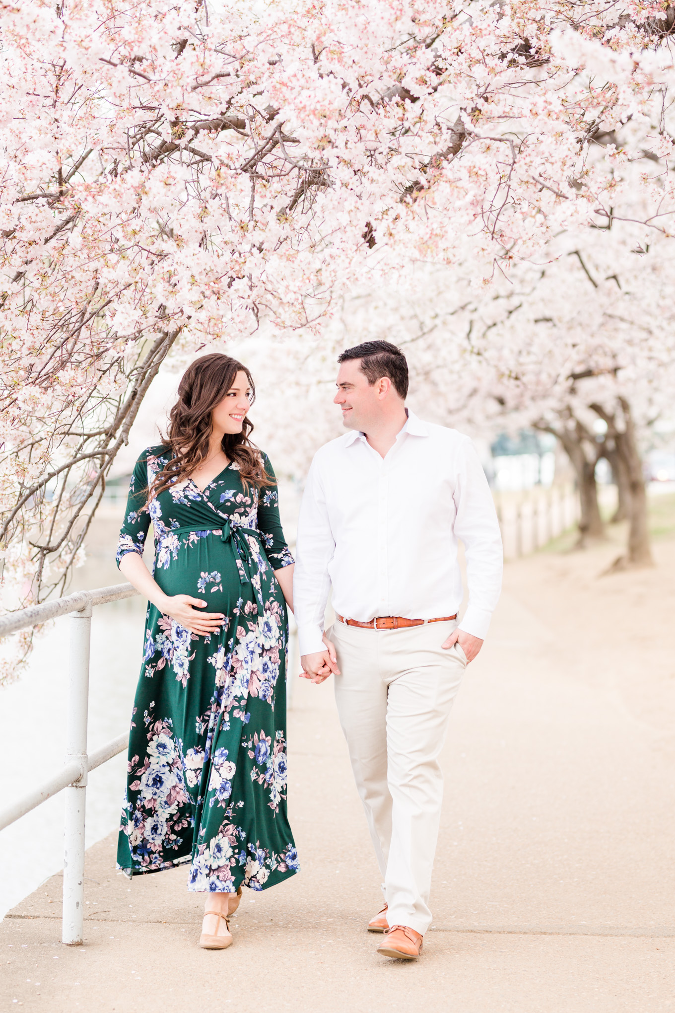 D.C. cherry blossoms photographer, D.C. cherry blossoms maternity session, maternity portraits, maternity photos, D.C. cherry blossoms, cherry blossoms maternity photo, floral print dress, brunette expectant mom, expecting mother, brunette woman, pregnant woman, third trimester, baby bump, couple snuggling, cute couple, cherry blossom trees, couple walking, hands on baby bump