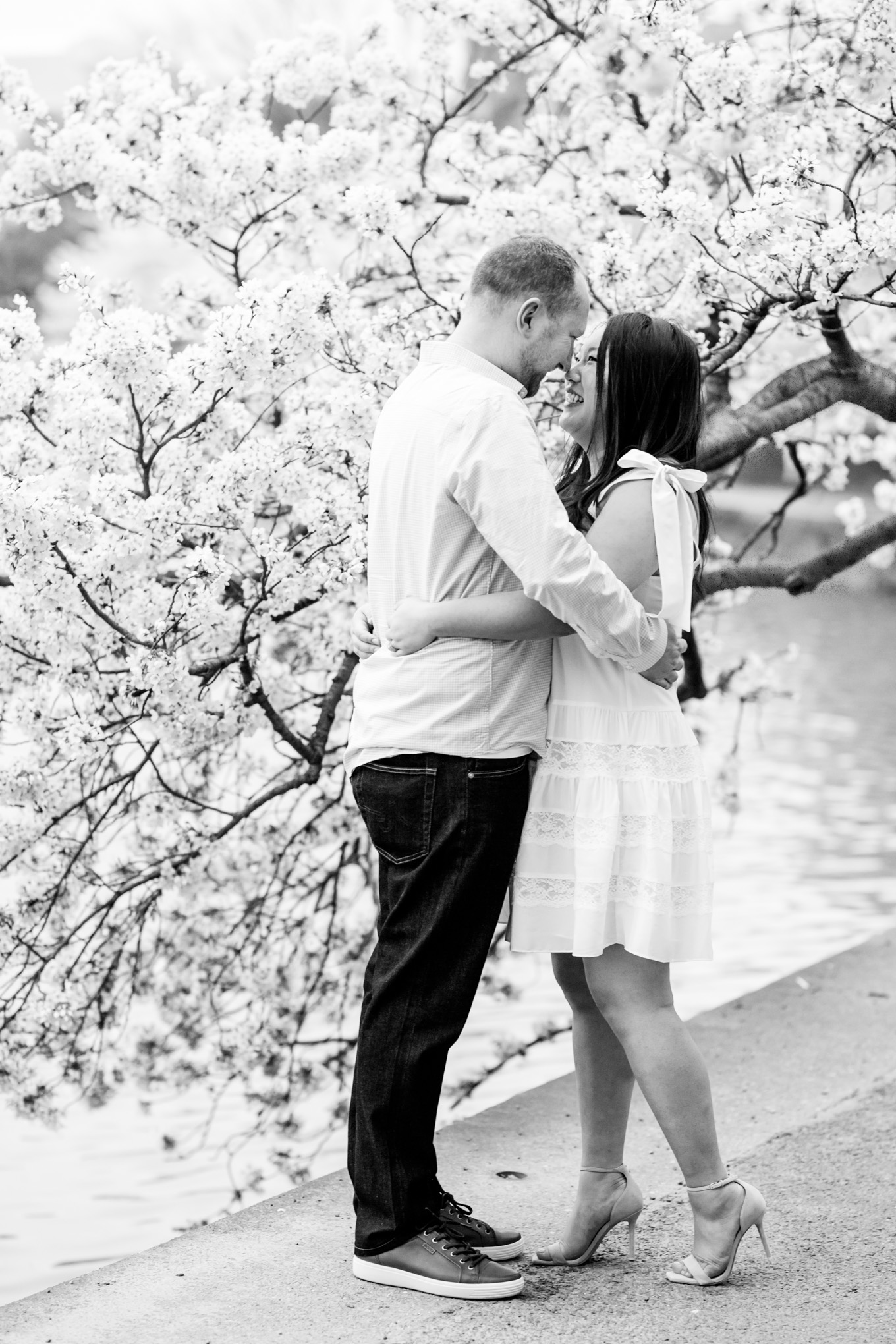 engaged couple, engagement portraits, photo shoot outfit ideas, cherry blossom engagement portraits, cherry blossom portraits, cherry blossoms, DC cherry blossoms, tidal basin, DC tidal basin, white cotton dress, white cotton sleeveless dress, bow sleeves, black and white photo, classic cherry blossom engagement session, D.C. engagement photographer