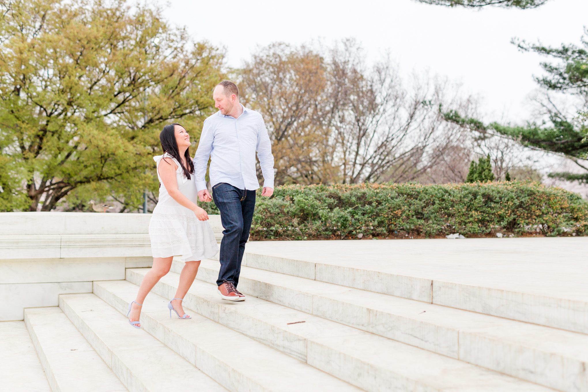engaged couple, engagement portraits, photo shoot outfit ideas, cherry blossom engagement portraits, cherry blossom portraits, cherry blossoms, DC cherry blossoms, tidal basin, DC tidal basin, white cotton dress, white cotton sleeveless dress, bow sleeves, classic cherry blossom engagement session, Washington Monument, Jefferson Memorial, Jefferson Memorial engagement photos, engagement ring, D.C. engagement photographer, couple walking