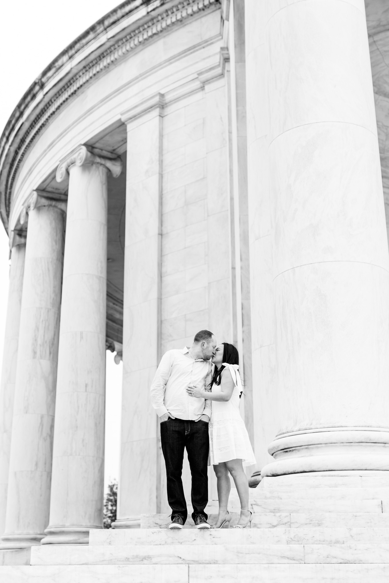 engaged couple, engagement portraits, photo shoot outfit ideas, cherry blossom engagement portraits, cherry blossom portraits, cherry blossoms, DC cherry blossoms, tidal basin, DC tidal basin, white cotton dress, white cotton sleeveless dress, bow sleeves, classic cherry blossom engagement session, Jefferson Memorial, Jefferson Memorial engagement photos, black and white photo, black and white engagement photo, D.C. engagement photographer