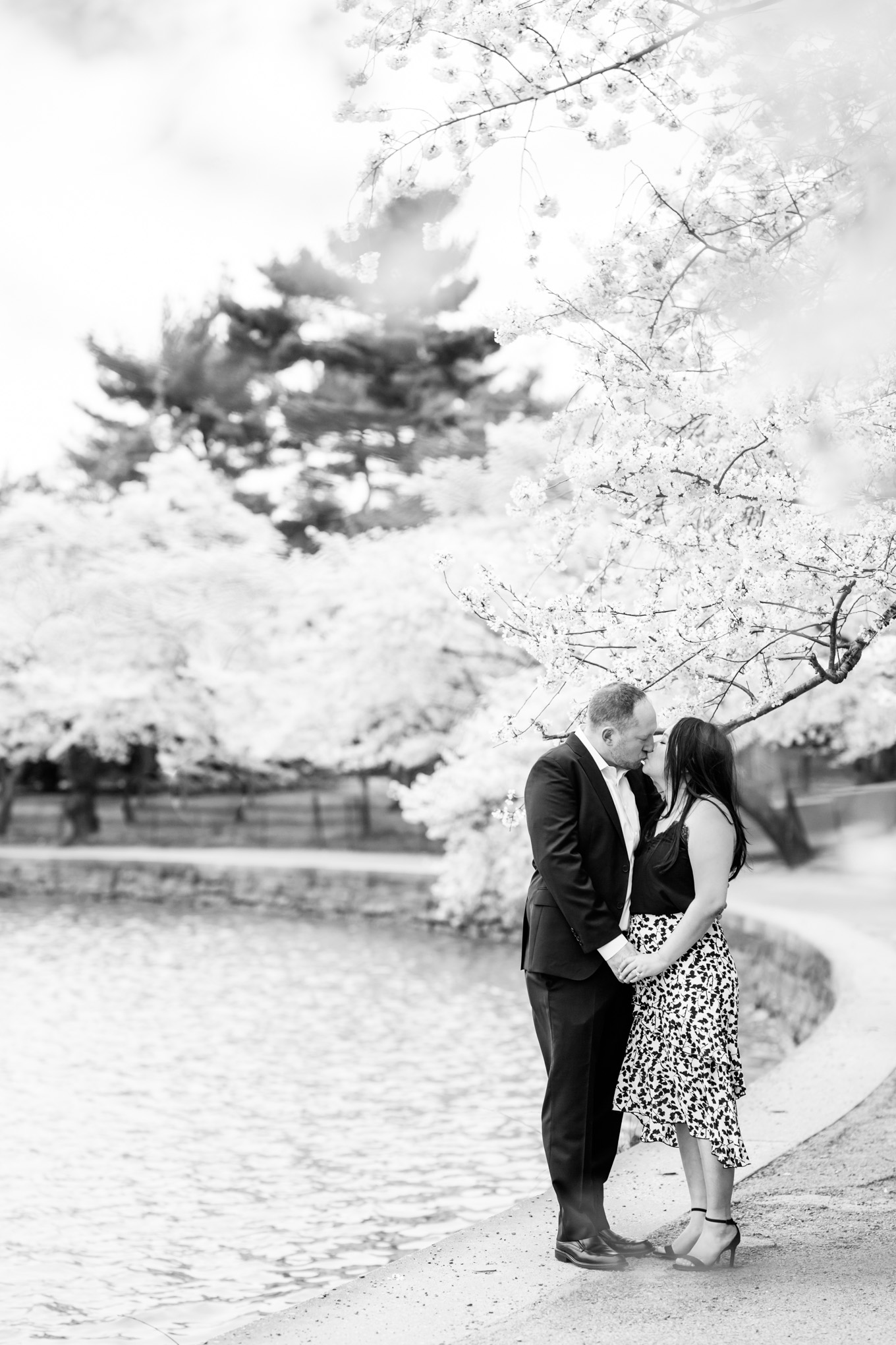 engaged couple, engagement portraits, photo shoot outfit ideas, cherry blossom engagement portraits, cherry blossom portraits, cherry blossoms, DC cherry blossoms, tidal basin, DC tidal basin, white cotton dress, white cotton sleeveless dress, bow sleeves, classic cherry blossom engagement session, D.C. engagement photographer, cherry blossom trees, floral print skirt, black and navy outfit, black and white outfit, black and white photo