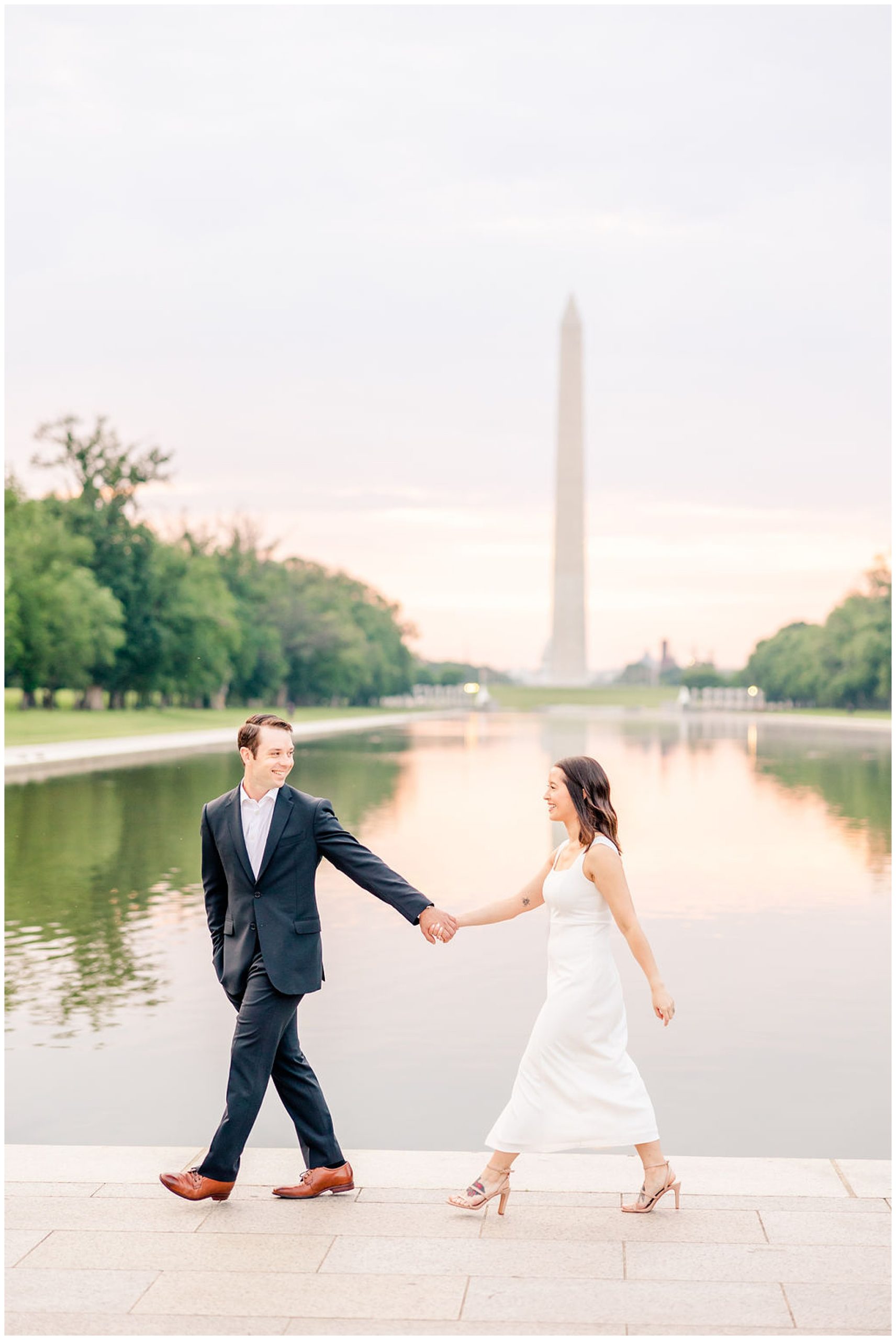 pink sunrise Lincoln Memorial engagement, DC engagement session, DC engagement photographer, formal DC engagement photos, DC elopement photographer, DC wedding photographer, classic DC engagement photos, luxury DC engagement photographer, Rachel E.H. Photography, couple holding hands from distance, couple walking along water, man looking at fiancé
