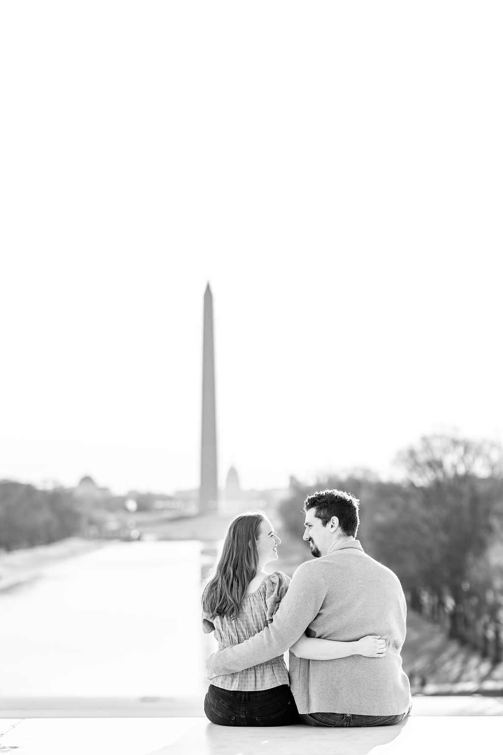 peak bloom cherry blossoms engagement, cherry blossoms engagement photos, DC peak bloom cherry blossoms, DC cherry blossoms photography, DC cherry blossoms photographer, ethereal cherry blossoms photos, DC cherry blossoms, Rachel E.H. Photography, black and white, couple looking at each other, couple sitting, couple with arms around each other, blue off the shoulder blouse